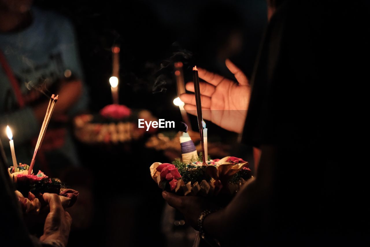 Cropped hands holding cake with candles at night
