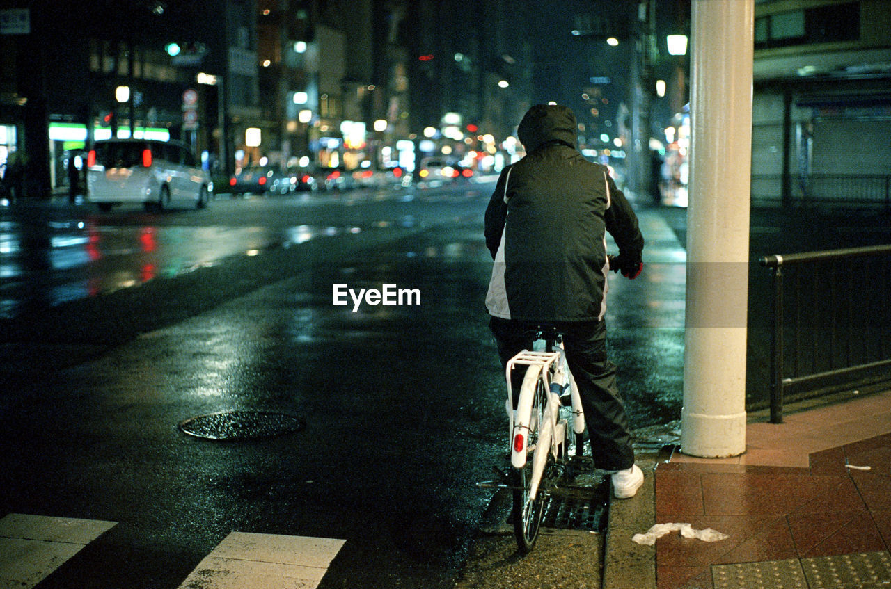 Rear view of man sitting on bicycle at road in city during night