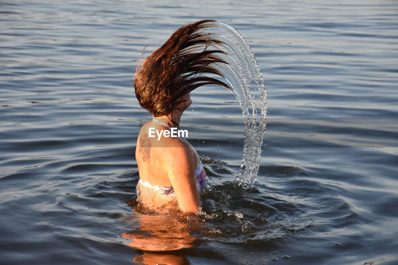 Side view of woman splashing water from hair in lake