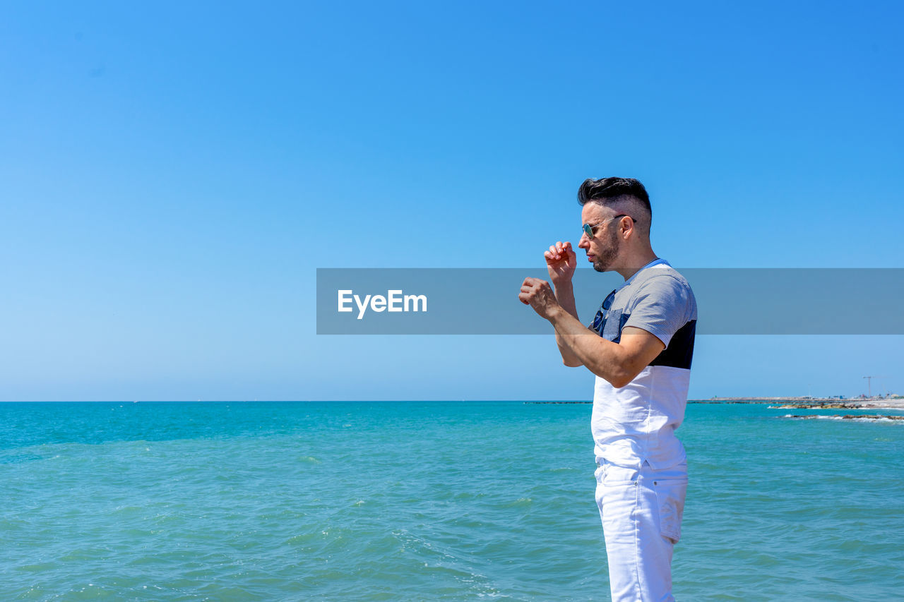 Side view of man standing at seashore against clear sky