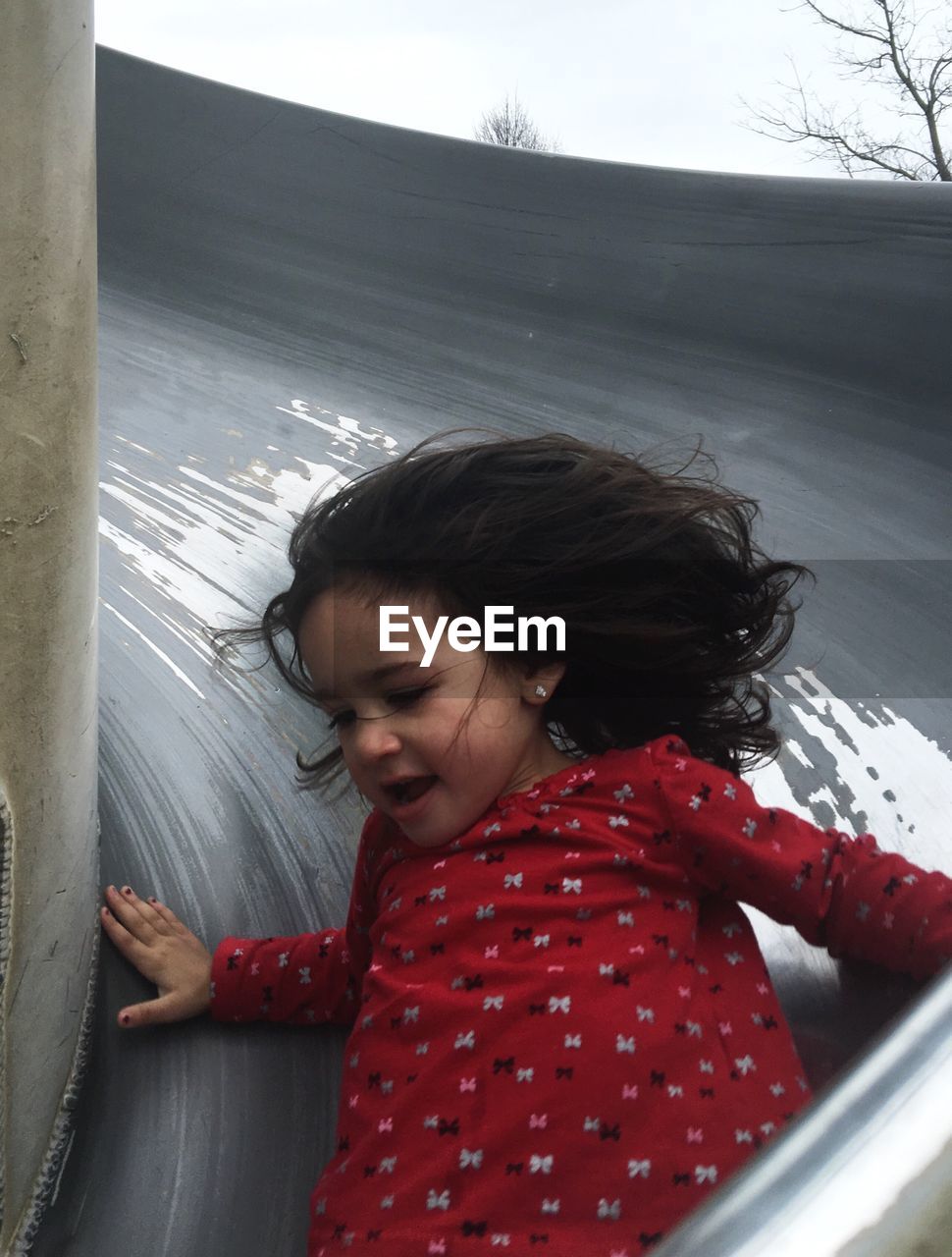 Low angle view of playful girl sliding in playground