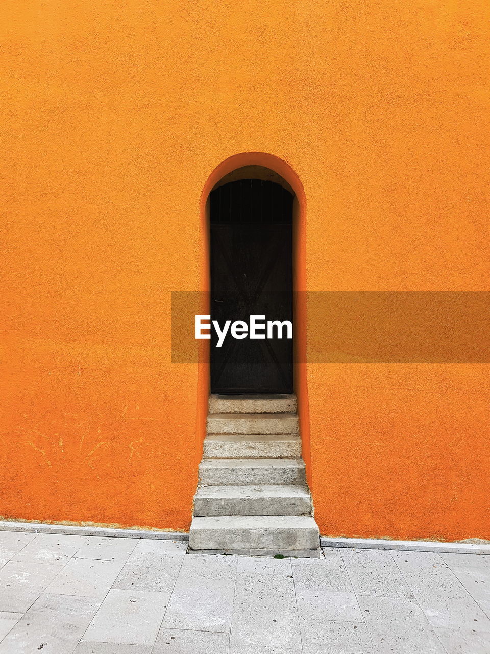Architectural minimalism, orange wall, stairs and dark door.