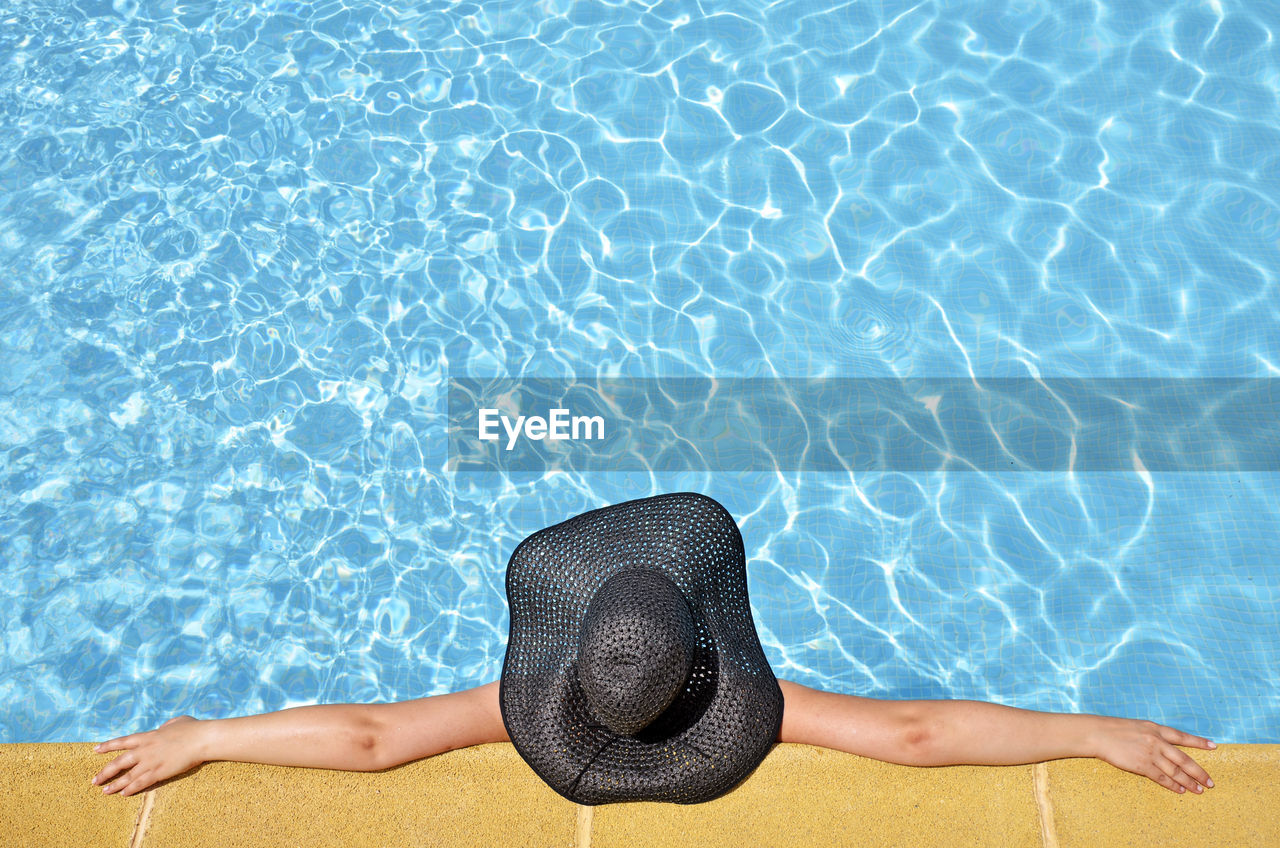 Directly above shot of woman with black hat relaxing in swimming pool