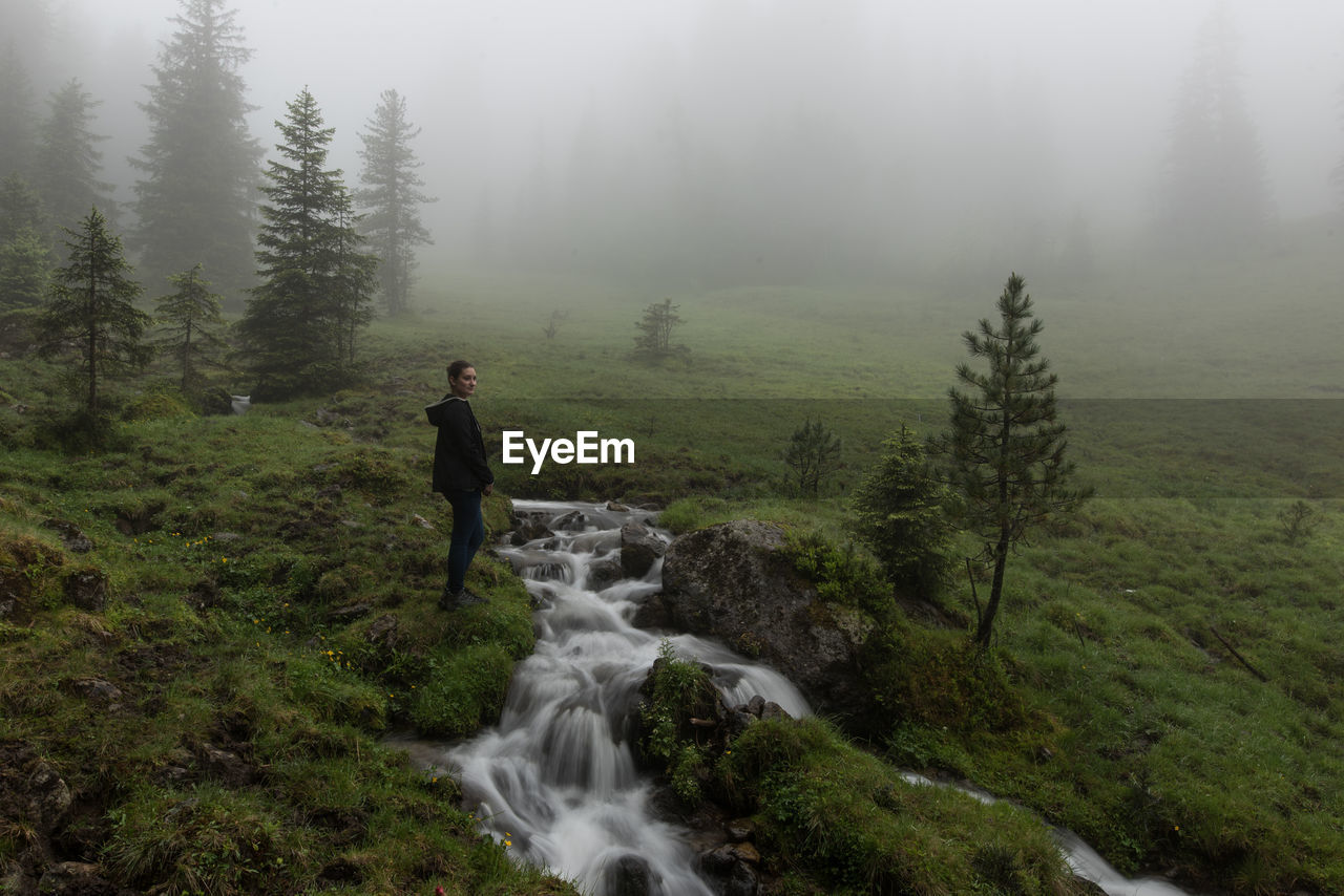 Side view of woman standing by stream during foggy weather