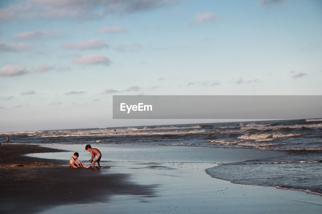 Full length of kids playing on beach against sky