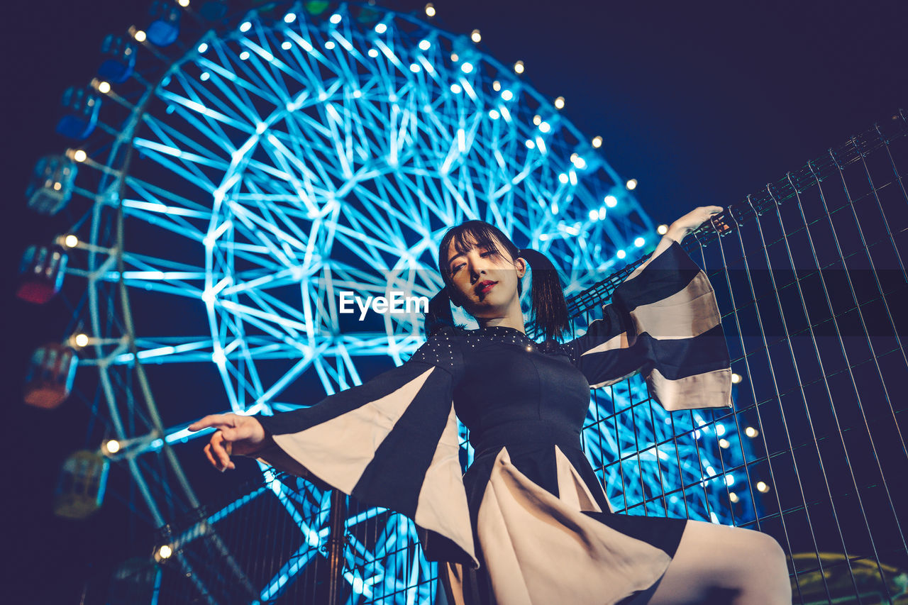 arts culture and entertainment, amusement park ride, one person, amusement park, adult, night, ferris wheel, young adult, happiness, emotion, women, illuminated, enjoyment, smiling, leisure activity, portrait, person, sky, blue, low angle view, fun, clothing, motion, lifestyles, nature