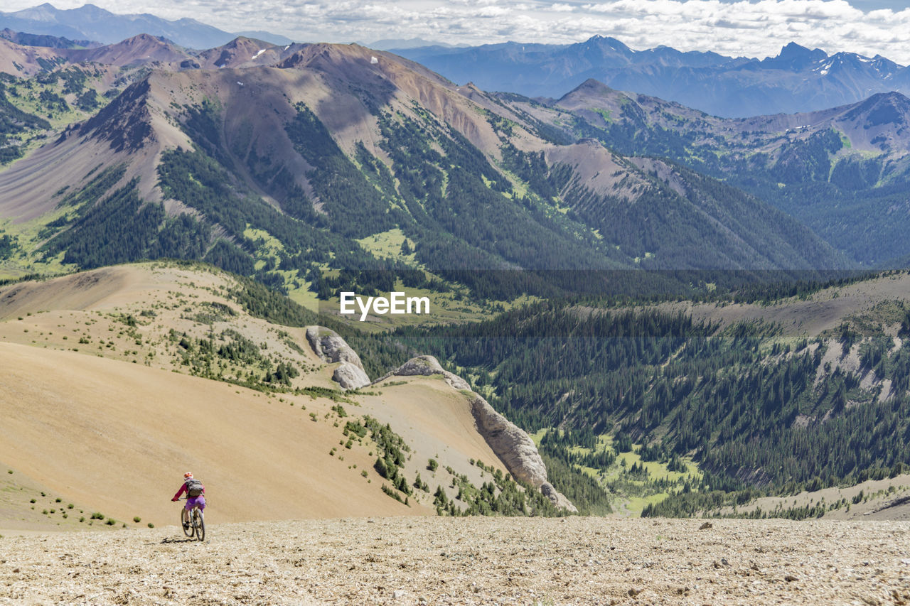 Rear view of man riding bicycle on field against mountain