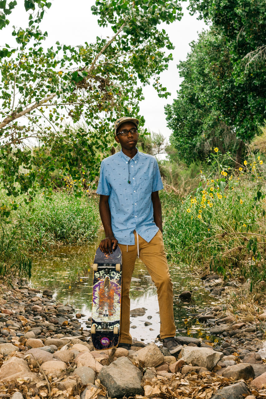 Man with skateboard standing by pond in forest