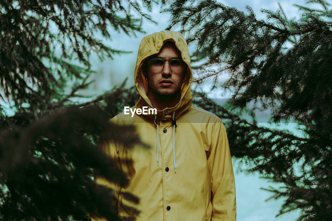 Portrait of young man wearing eyeglasses by pine tree