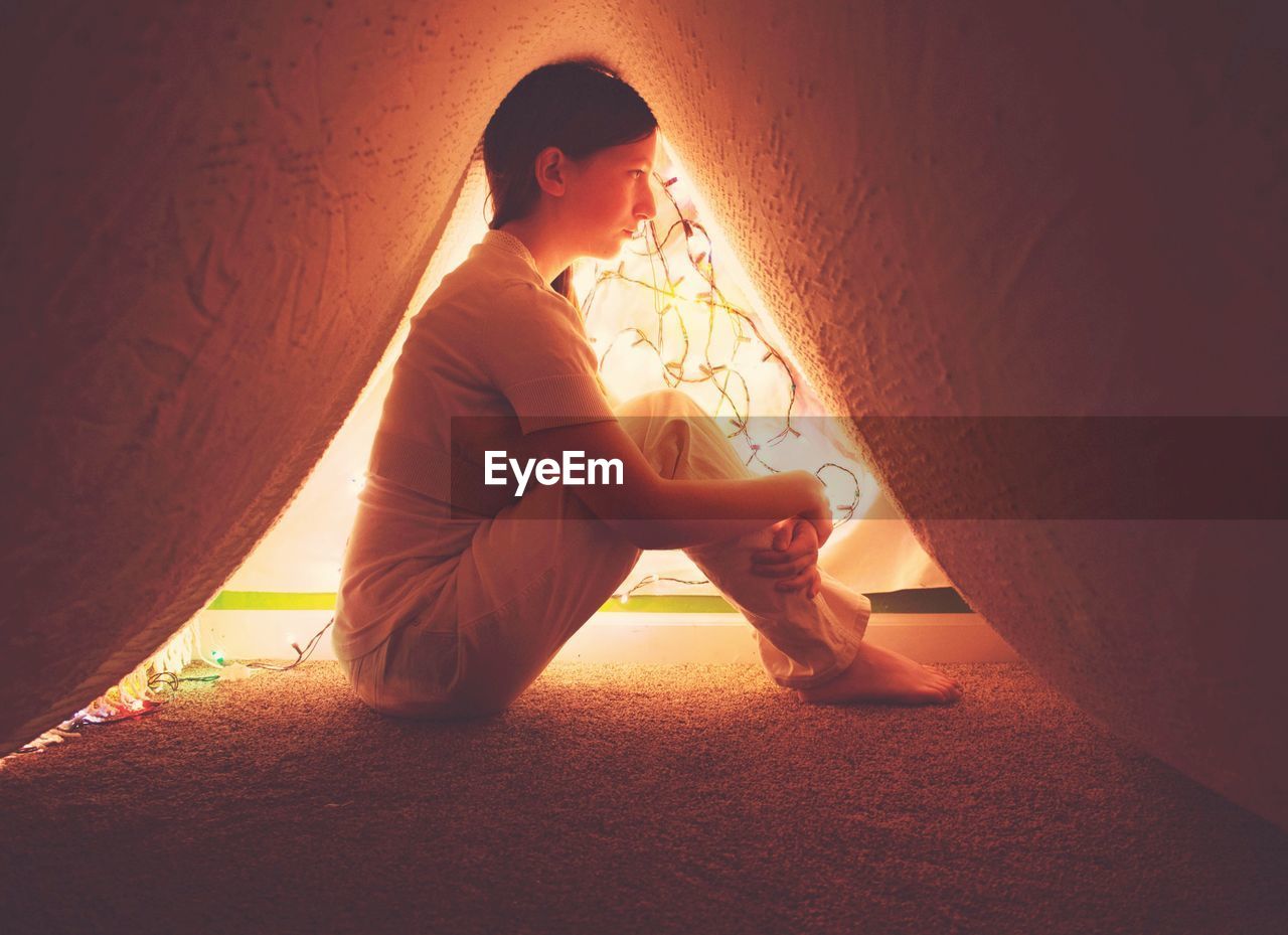 Side view of woman sitting under carpet at home