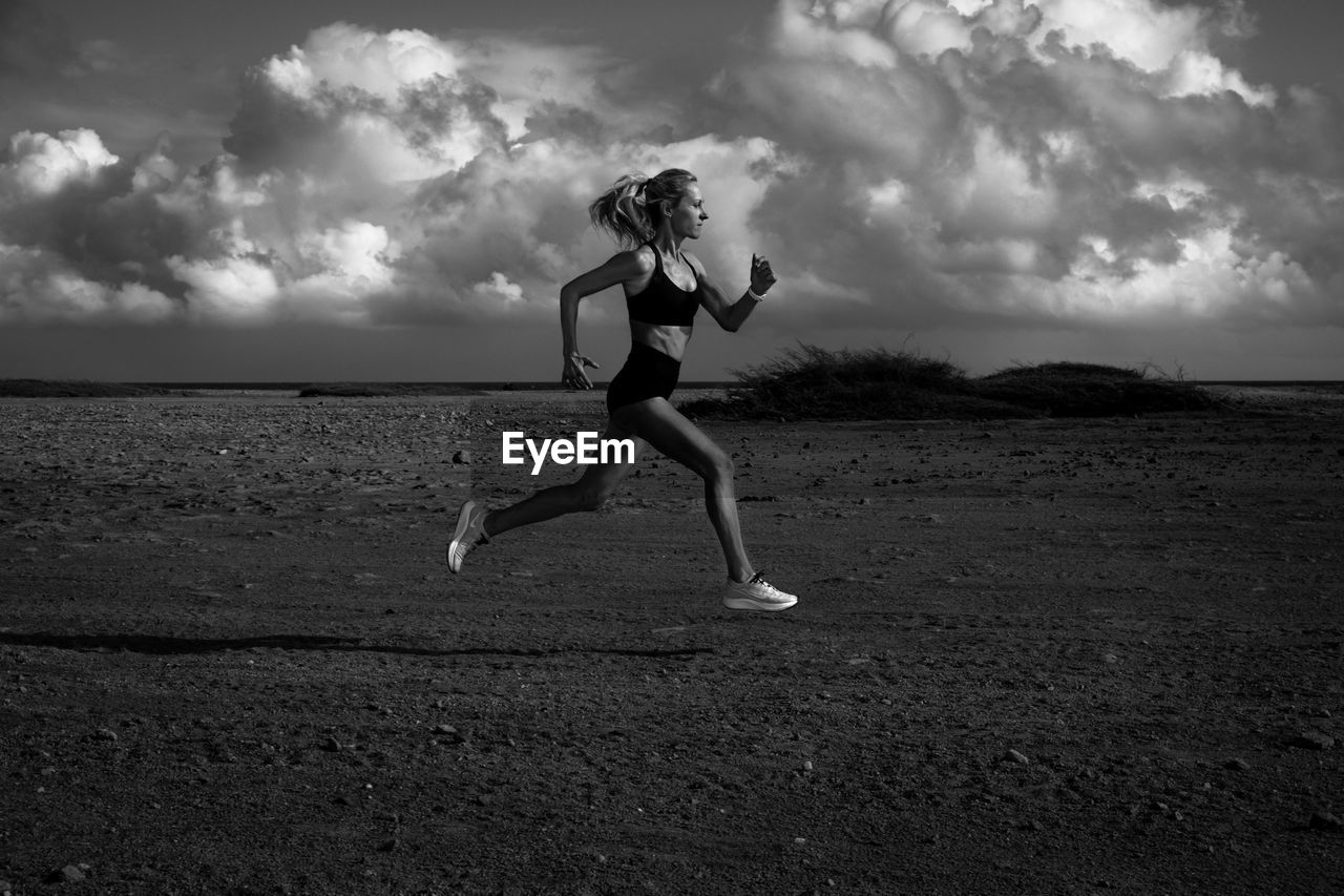 FULL LENGTH OF WOMAN RUNNING ON FIELD AGAINST SKY