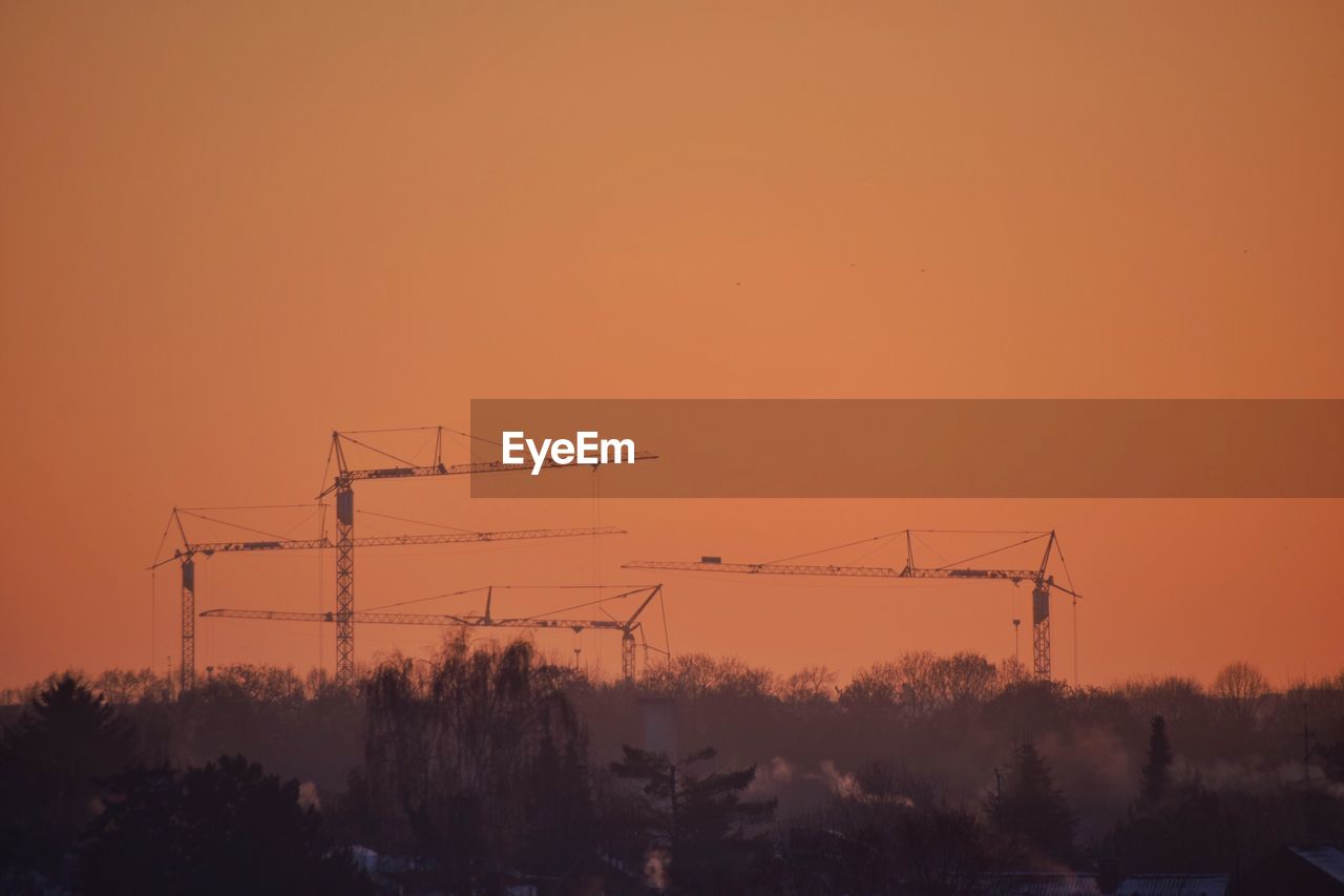 Silhouette of cranes against sky during sunset