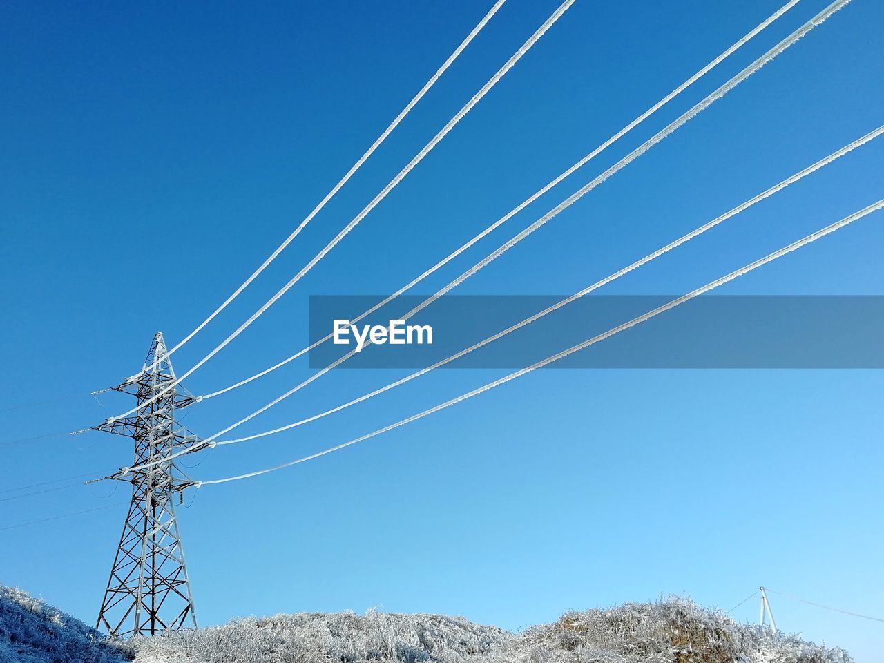 Low angle view of electricity pylon against blue sky