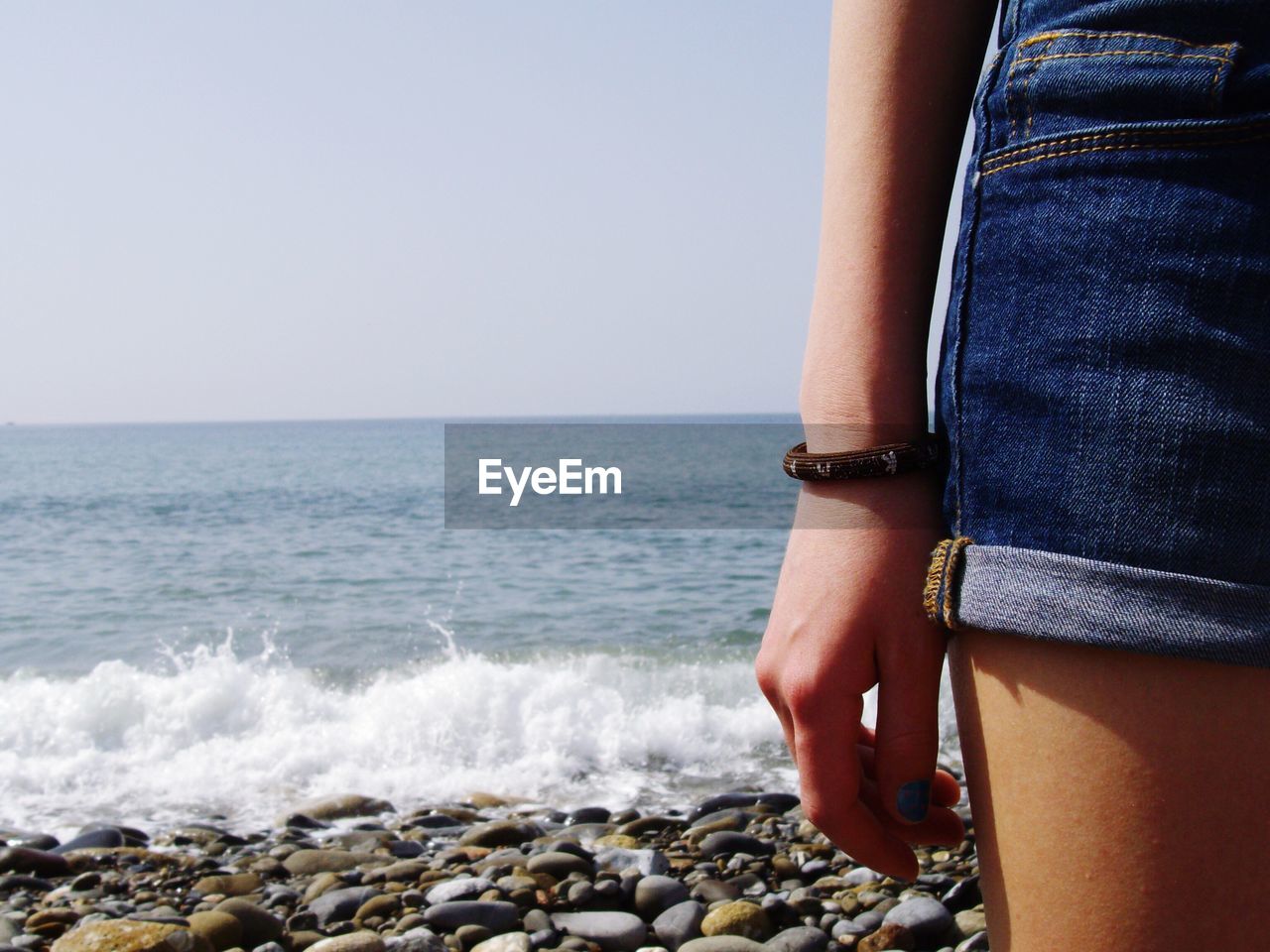 Midsection of woman standing at beach against clear sky