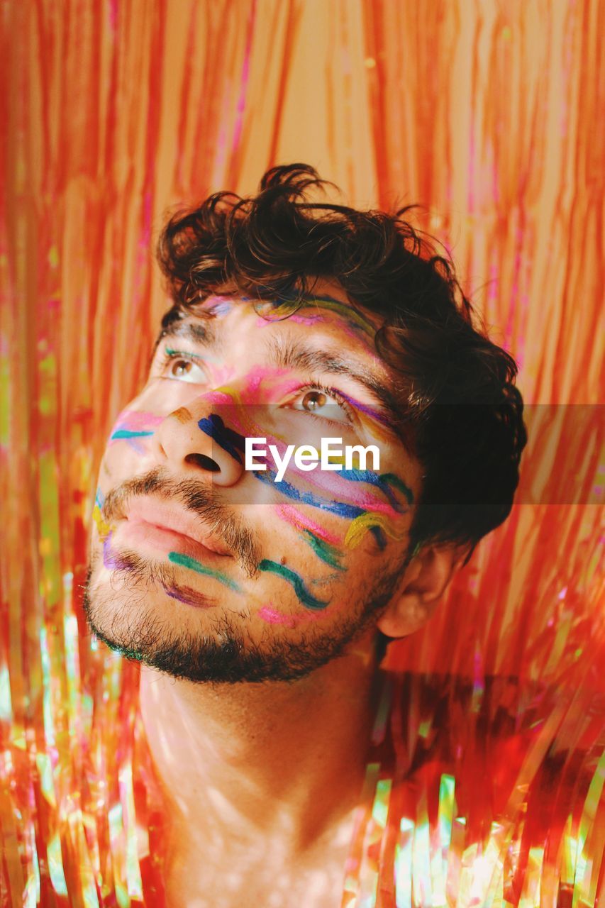 Queer young man in colorful face paint in glowing curtains at a party