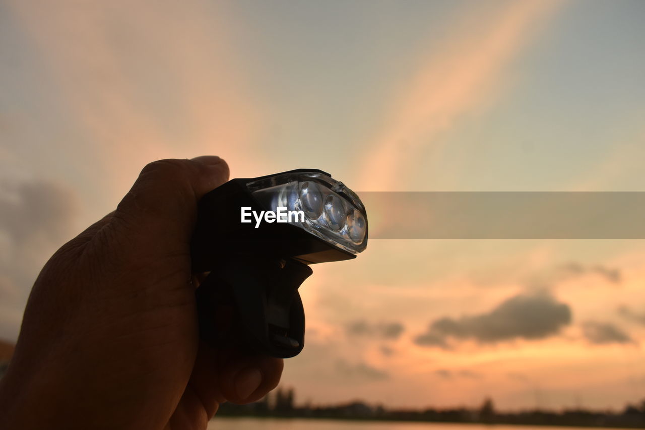 CLOSE-UP OF HAND HOLDING ORANGE AGAINST SKY