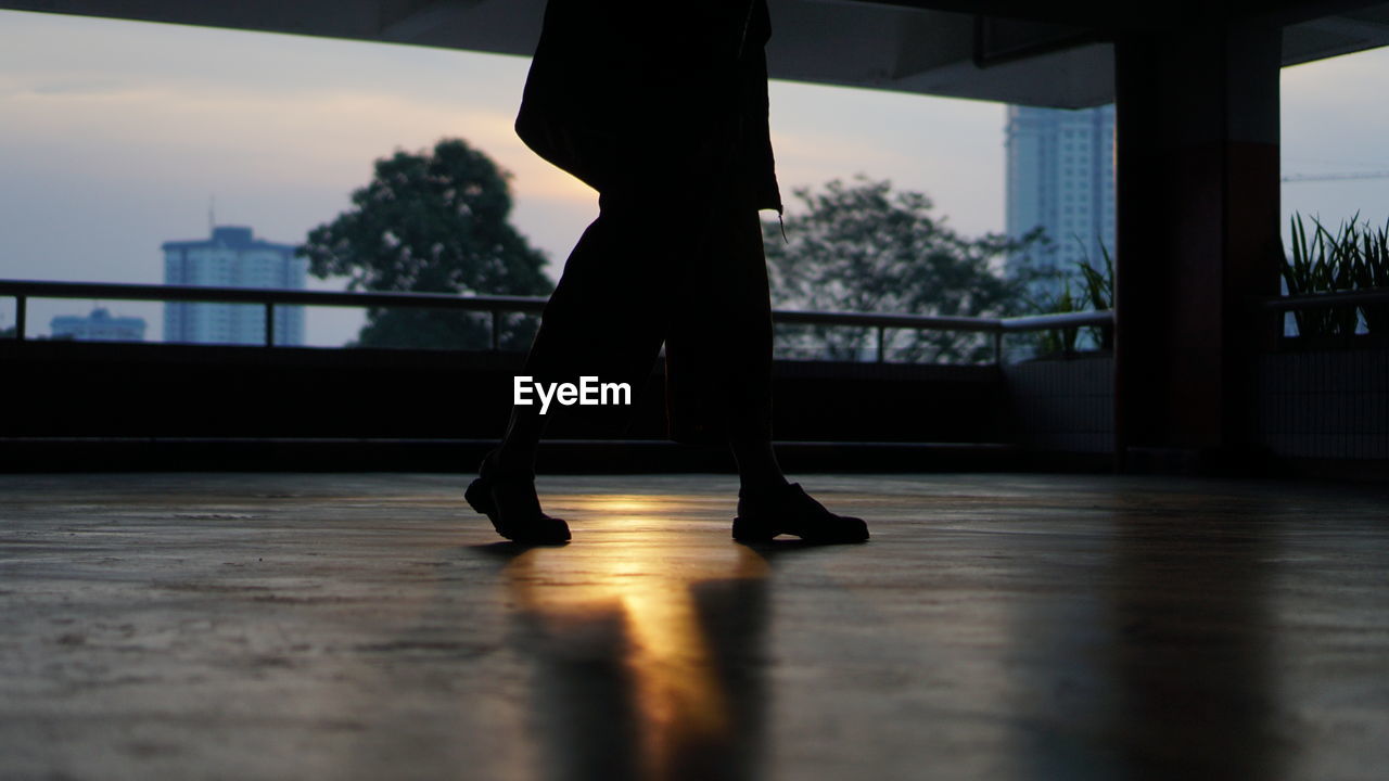 LOW SECTION OF SILHOUETTE WOMAN STANDING BY RAILING