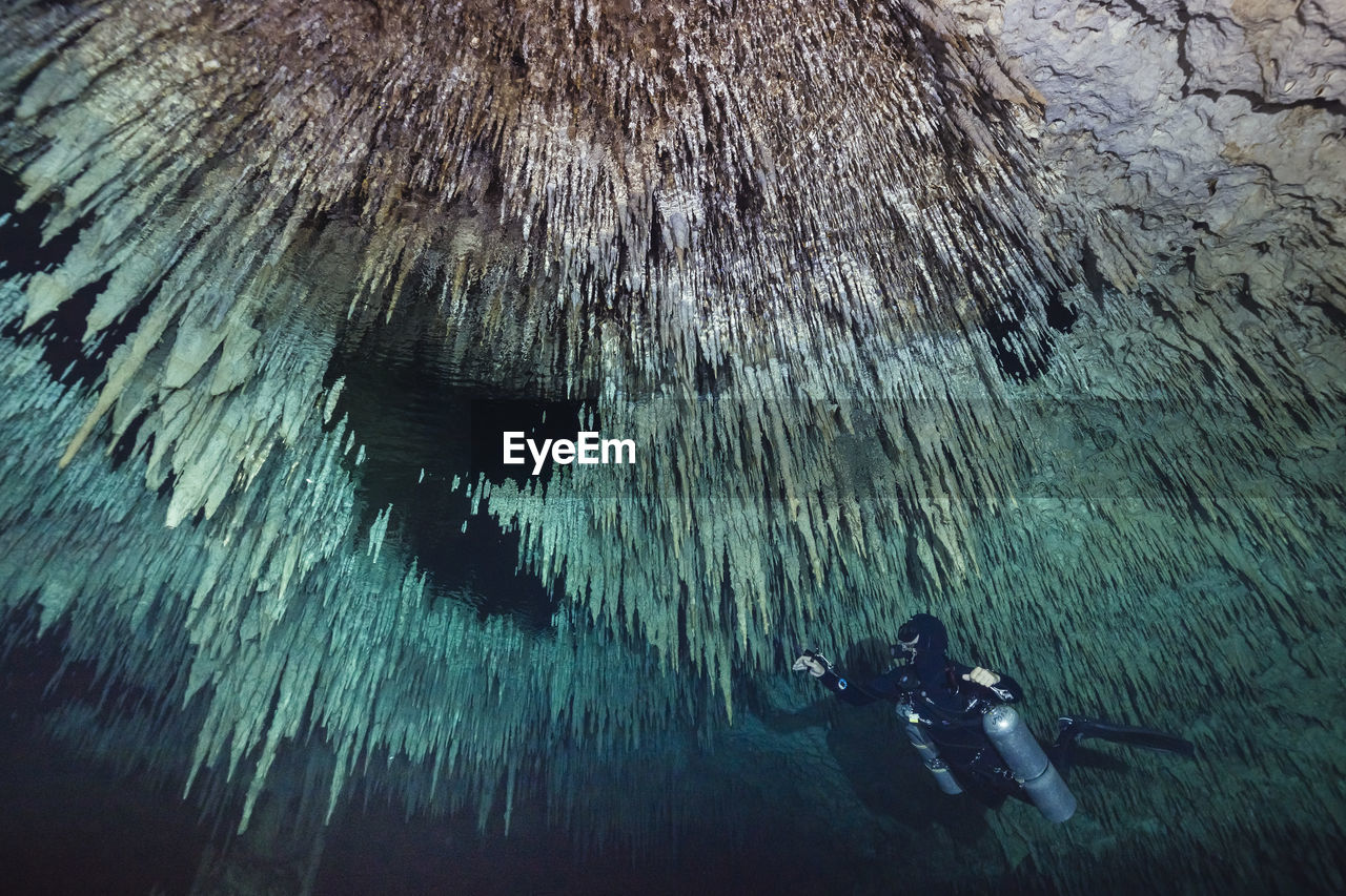 Low angle view of man scuba diving below stalactites in sea