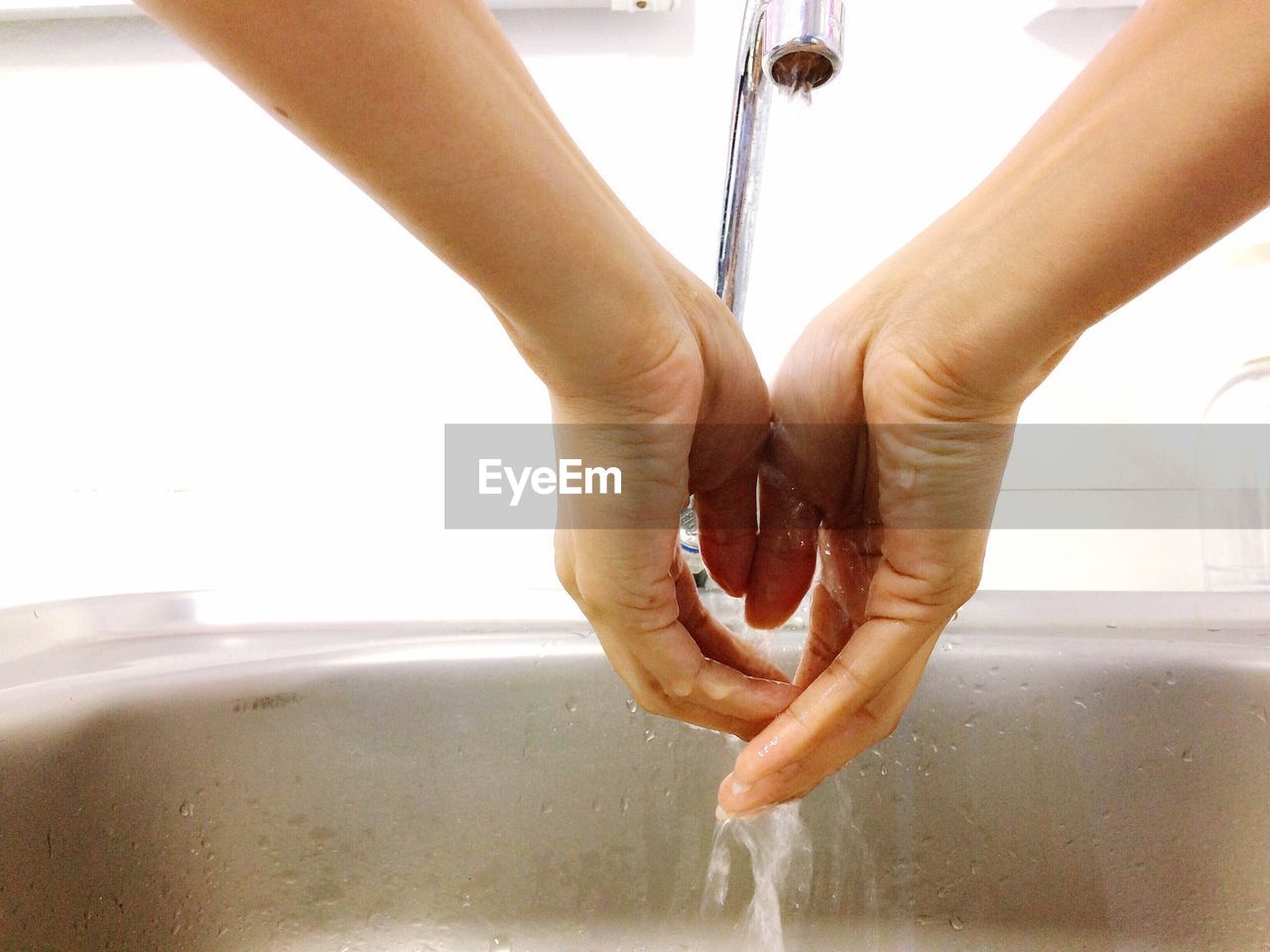 Close-up of woman washing hands below faucet in sink