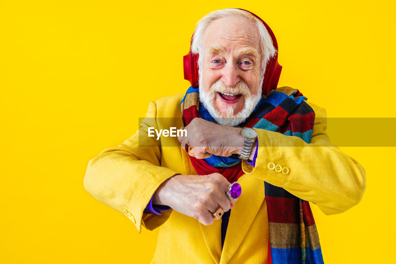 Senior man dancing while listening music against yellow background