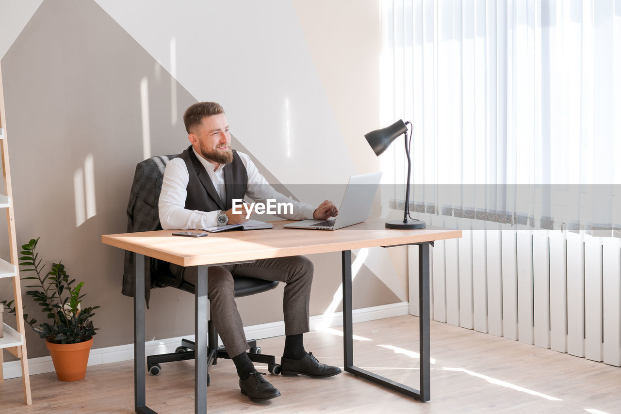 Caucasian bearded business man is sitting at window table using his laptop