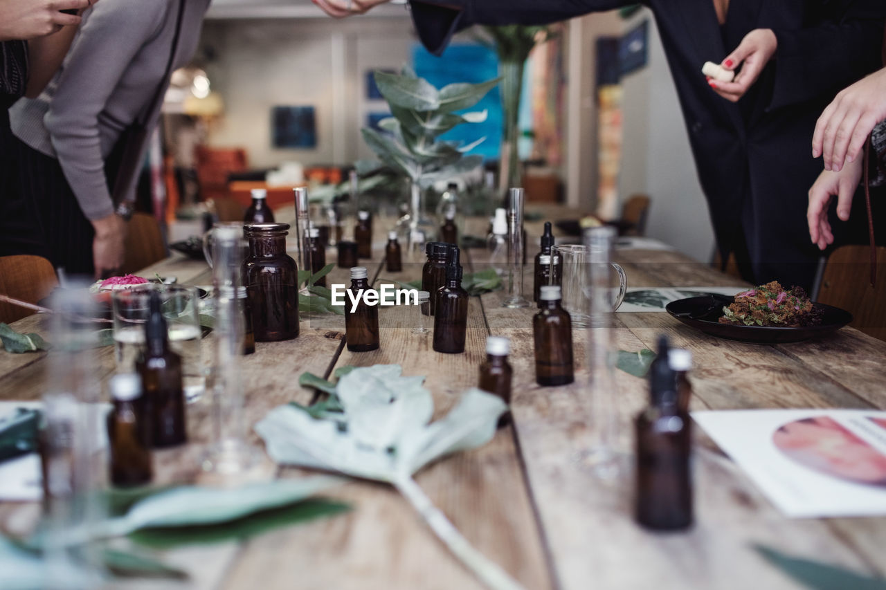 Various perfume bottles on table amidst female coworkers standing at workshop