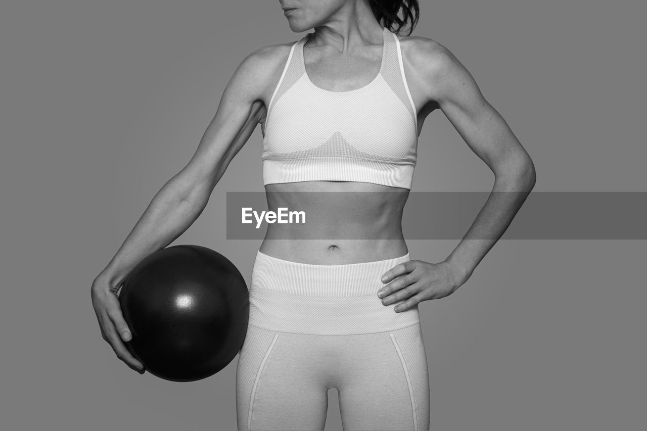 Fit woman standing holding a pilates ball, black and white.