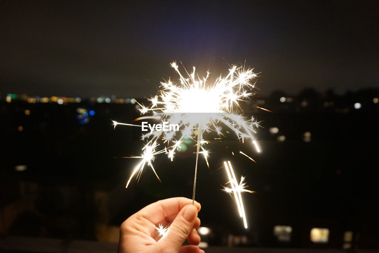 CLOSE-UP OF HAND HOLDING FIREWORK DISPLAY