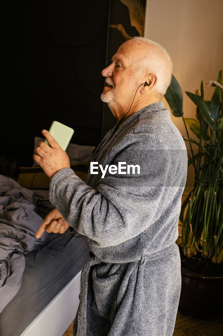 Side view of senior man dancing and listening music in bedroom at home