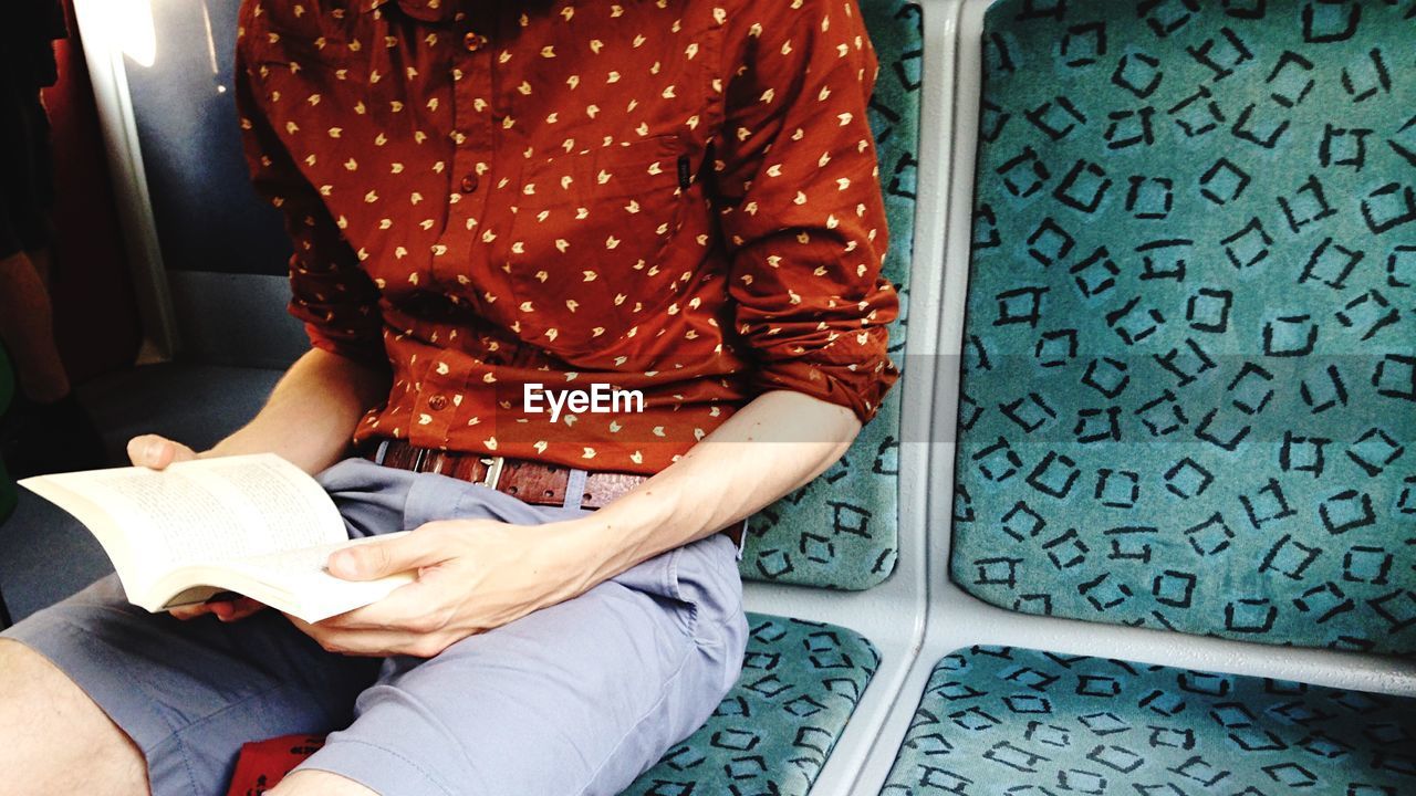 Midsection of man reading book while sitting in train