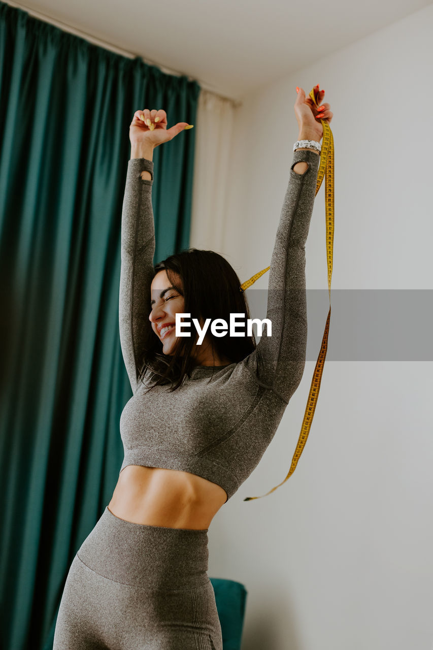 Young woman with arms raised standing against curtain