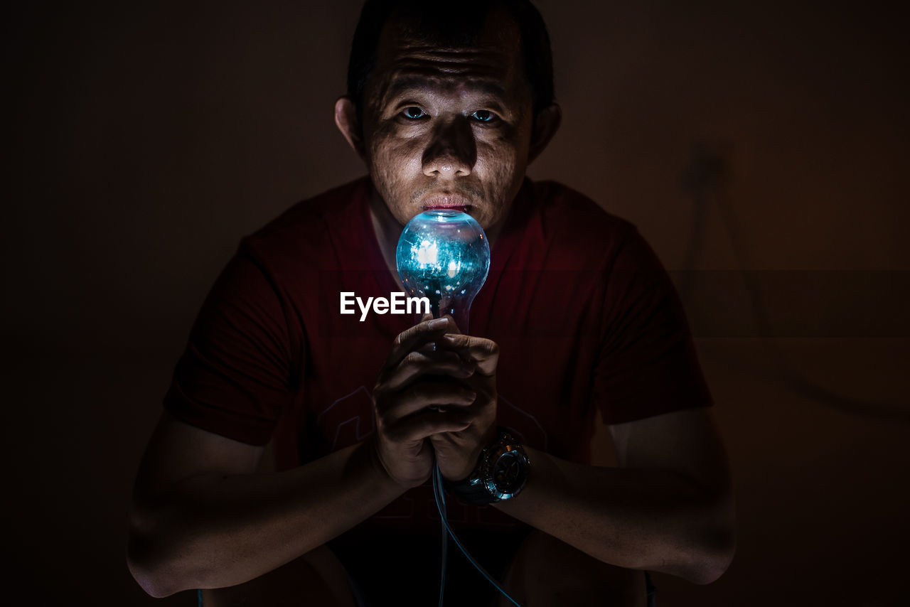 Close-up of man holding illuminated lighting equipment against wall