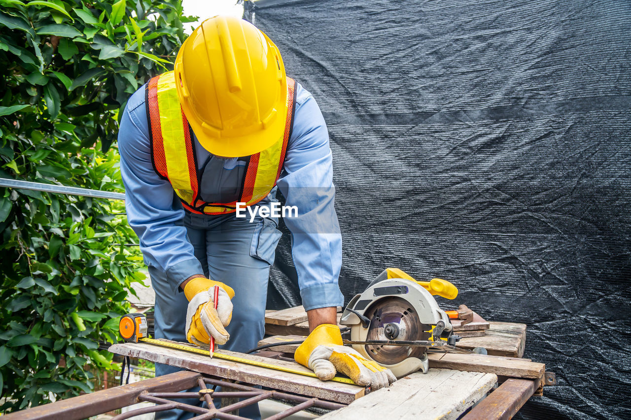 REAR VIEW OF MAN WORKING ON YELLOW UMBRELLA