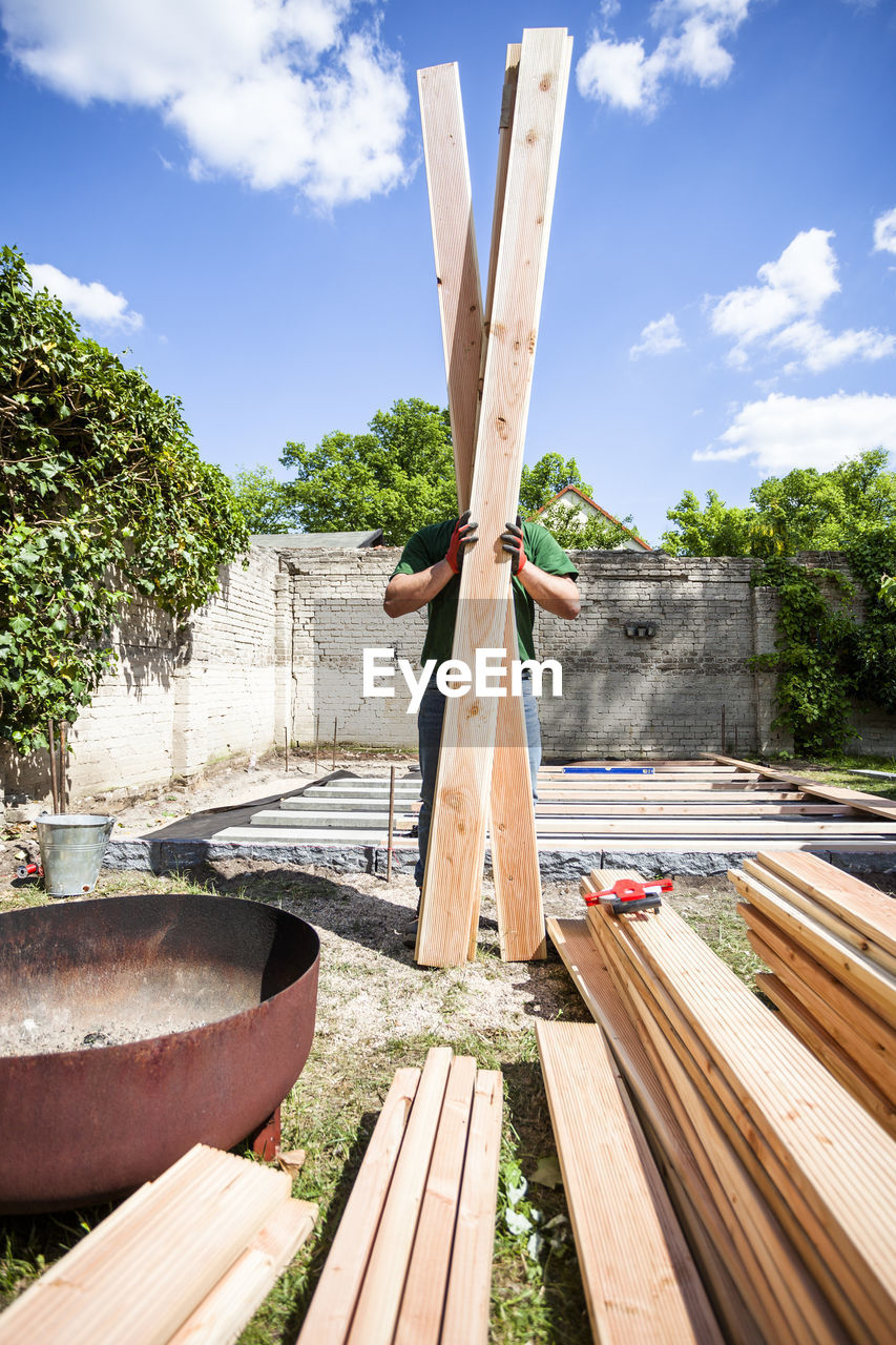 Man holding wooden planks at construction site against sky