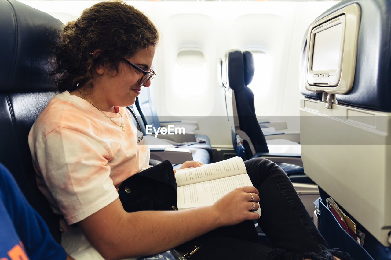 Smiling woman reading book while sitting in airplane