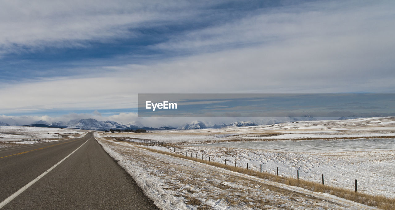 Empty road on snow covered landscape against sky