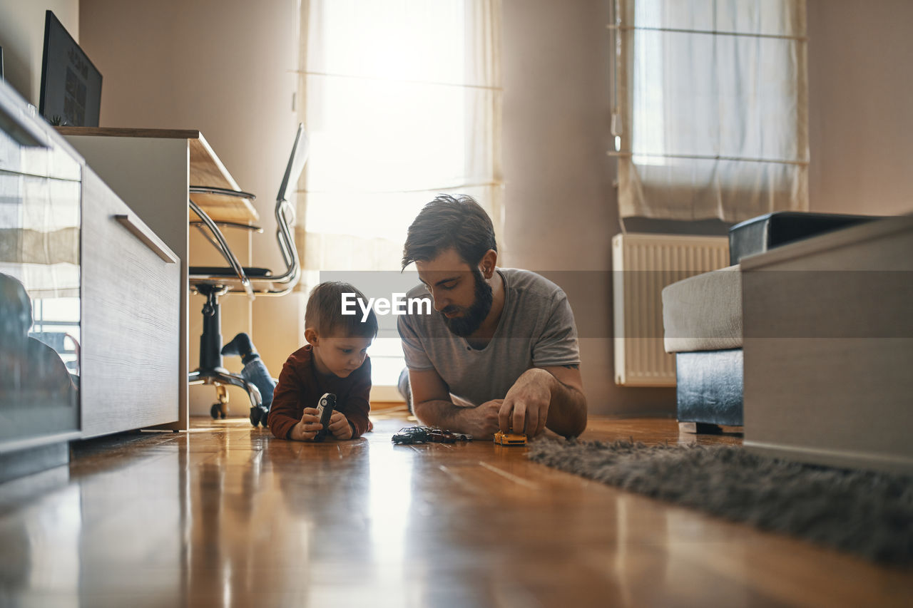 Father and son lying together on the floor playing with toy cars