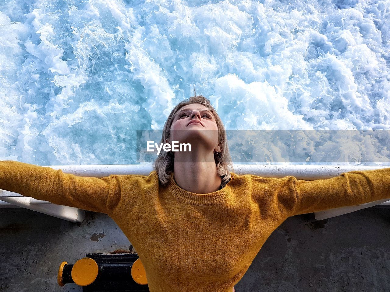 High angle view of young woman with arms outstretched standing by railing over sea