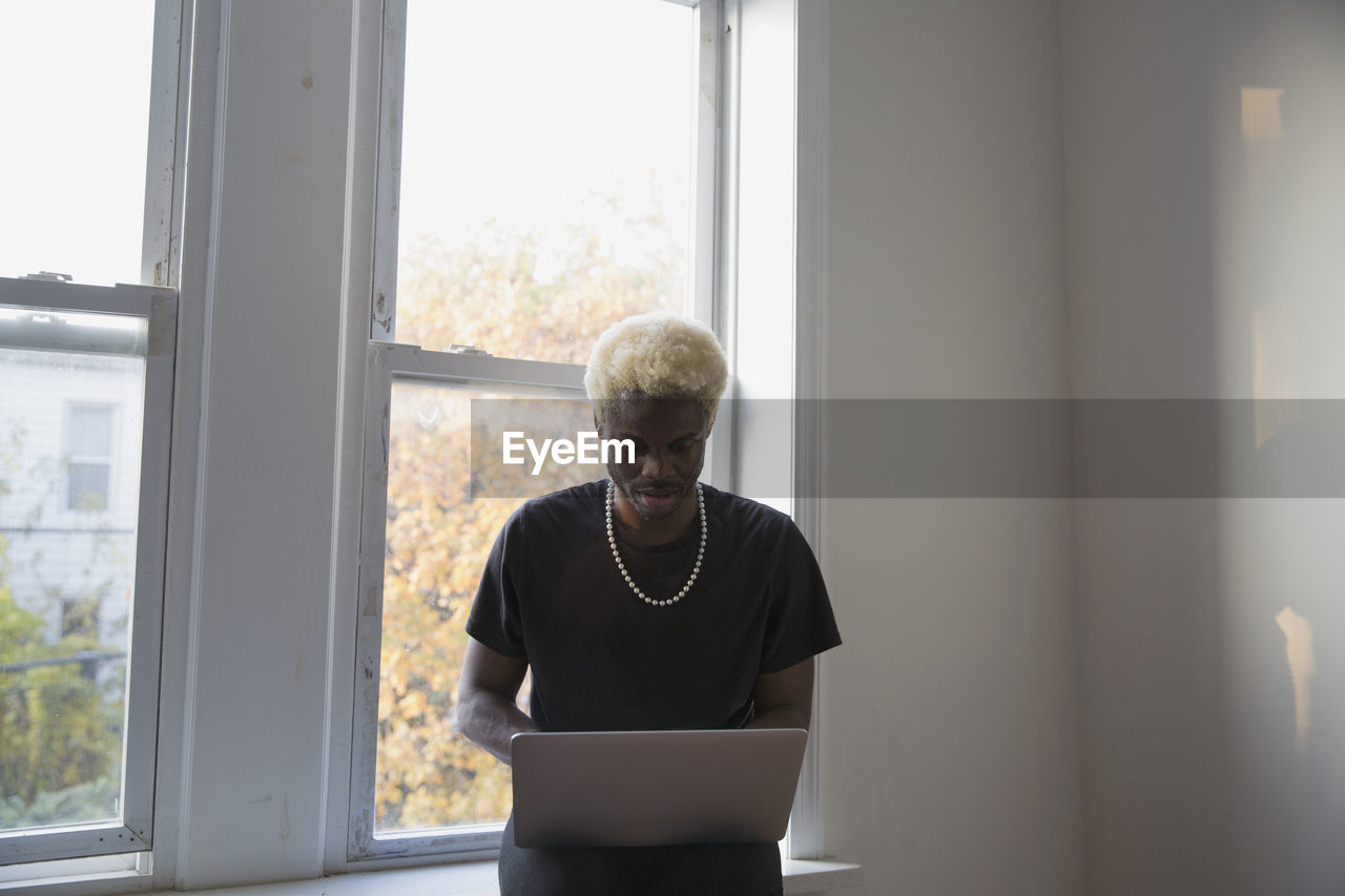 A young man with a laptop sitting on a windowsill