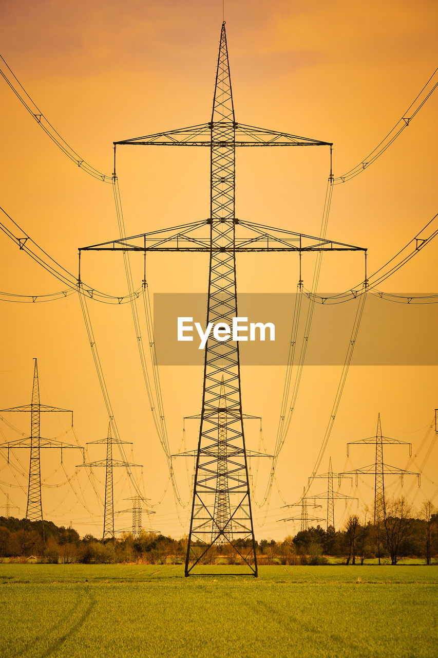 Low angle view of electricity pylon on field against sky during sunset