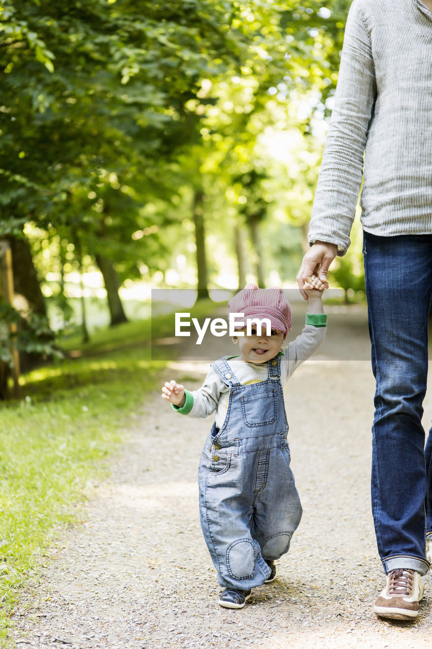 Portrait of baby girl holding mother's hand while walking on footpath