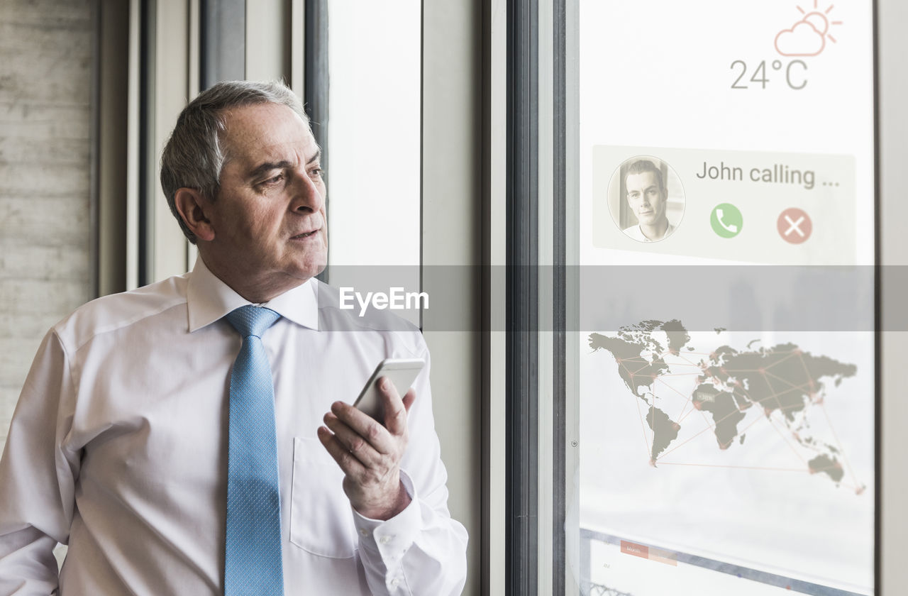 Businessman receiving a call on windowpane with world map in office