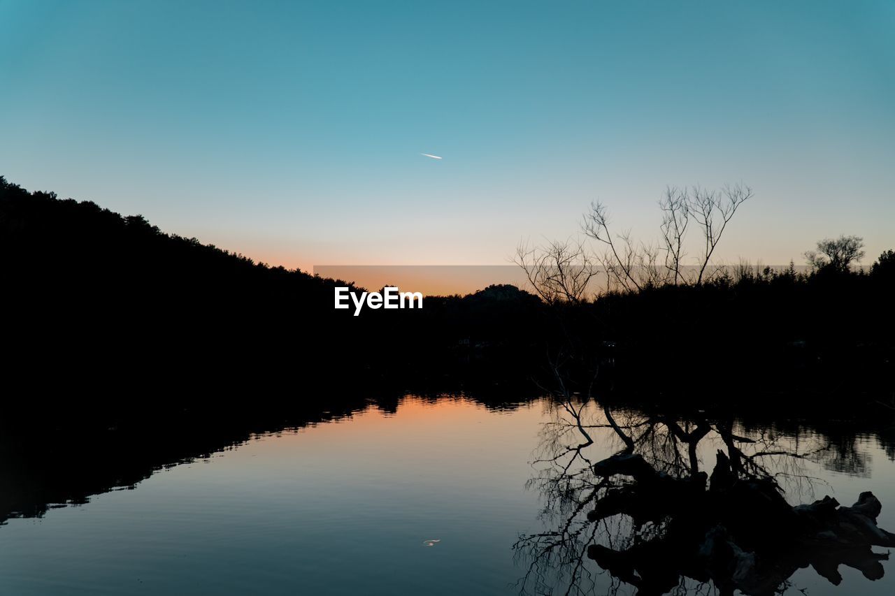 SILHOUETTE PLANTS BY LAKE AGAINST SKY DURING SUNSET