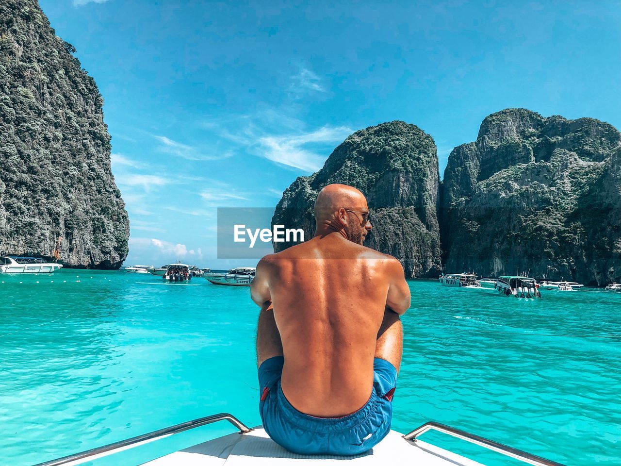 Rear view of shirtless man on boat in sea against sky