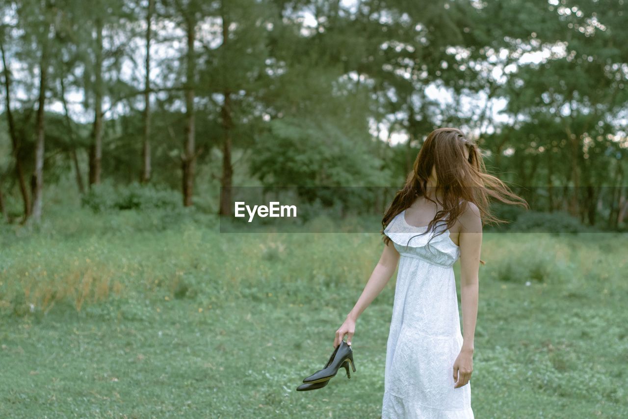 Woman holding shoes while standing on grassy field