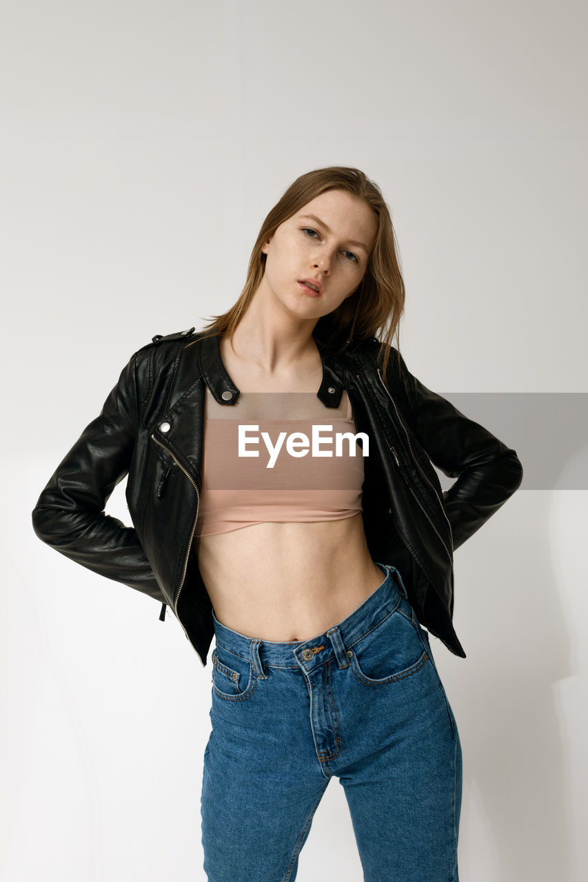 PORTRAIT OF BEAUTIFUL YOUNG WOMAN STANDING AGAINST GRAY BACKGROUND