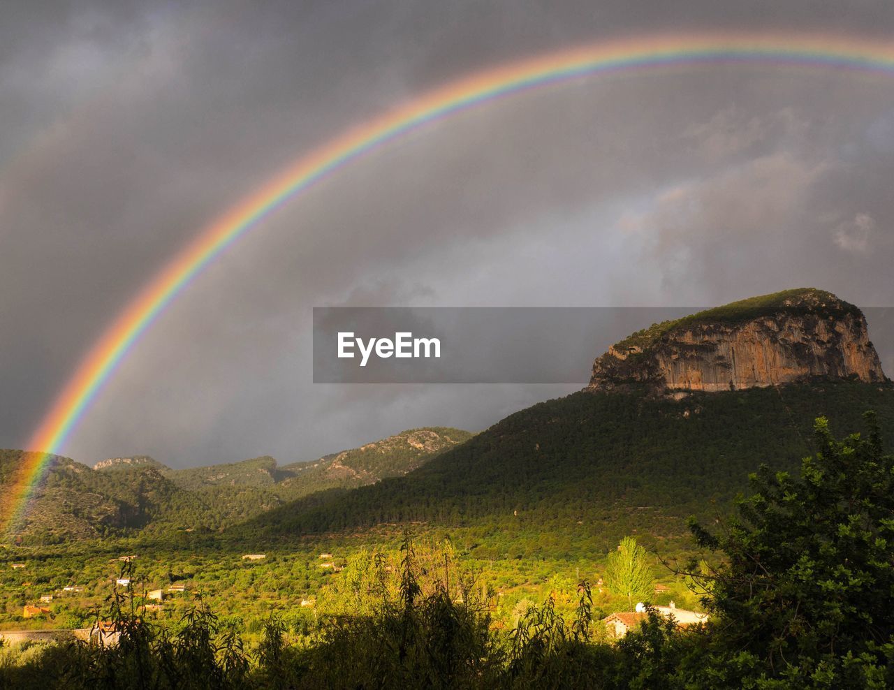 Scenic view of rainbow over mountain against dramatic sky