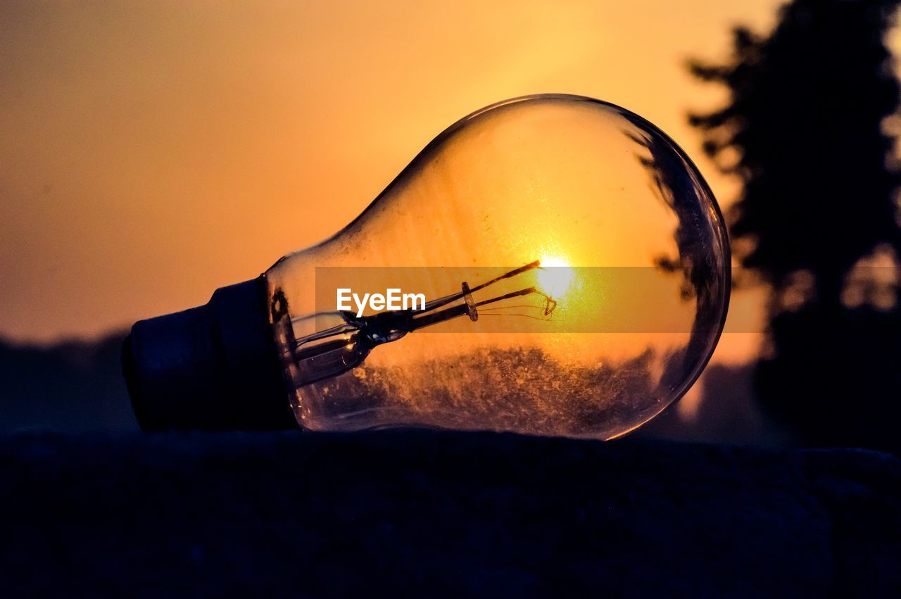 Close-up of illuminated light bulb against sky at sunset