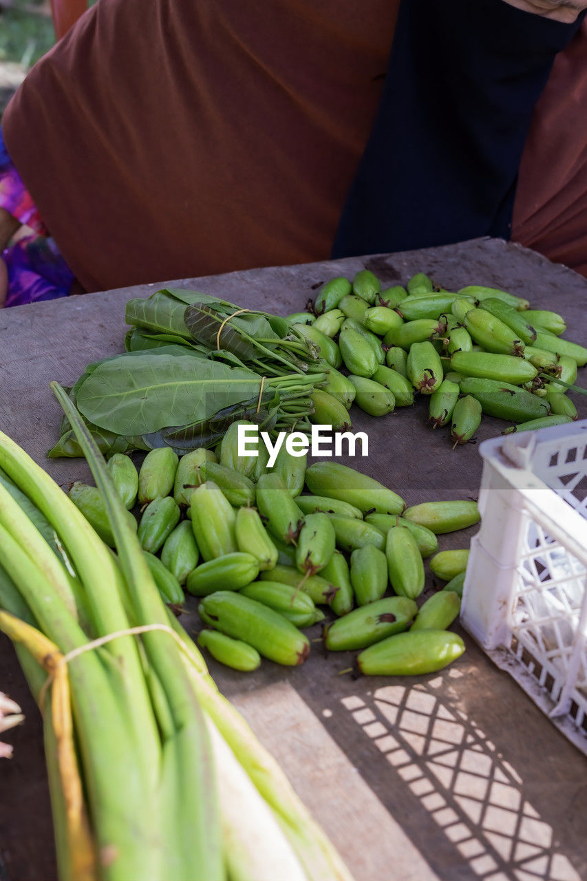 food, food and drink, healthy eating, vegetable, wellbeing, freshness, market, produce, one person, green, organic, adult, market stall, abundance, retail, business, raw food, day, large group of objects, holding, agriculture, midsection, high angle view, business finance and industry, asparagus, outdoors, small business, hand, crop