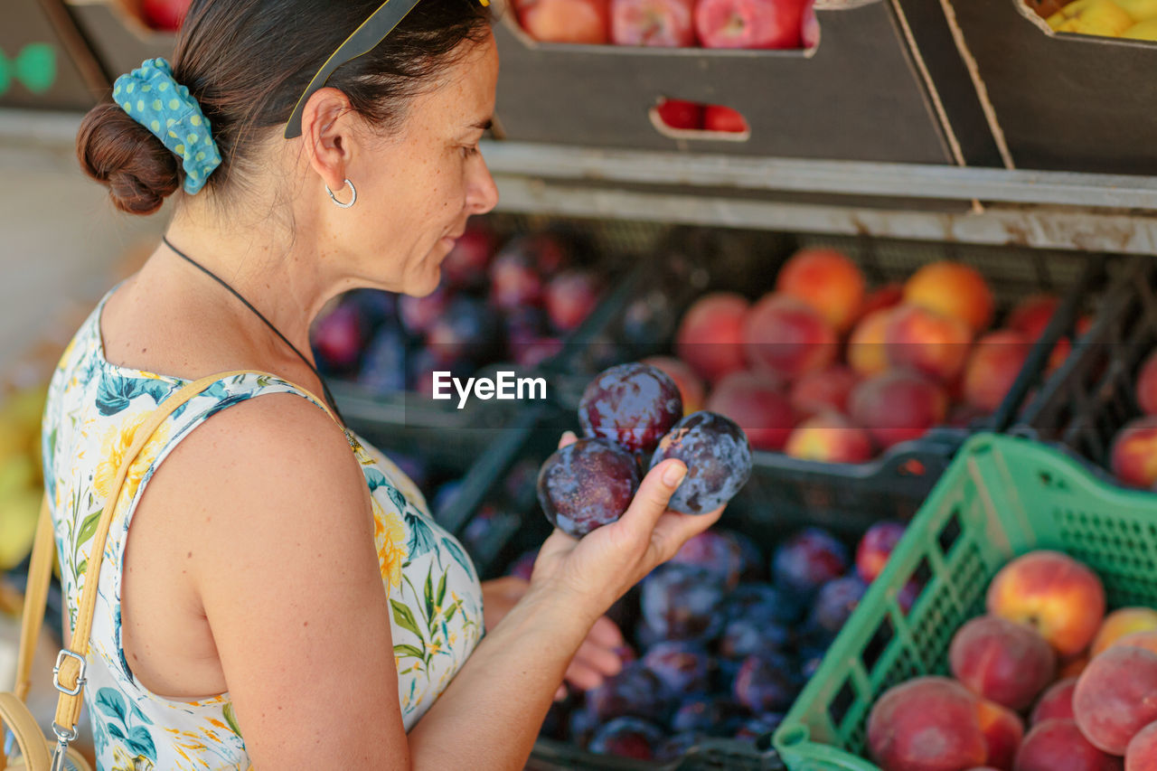 Mature woman choosing fruit in street store